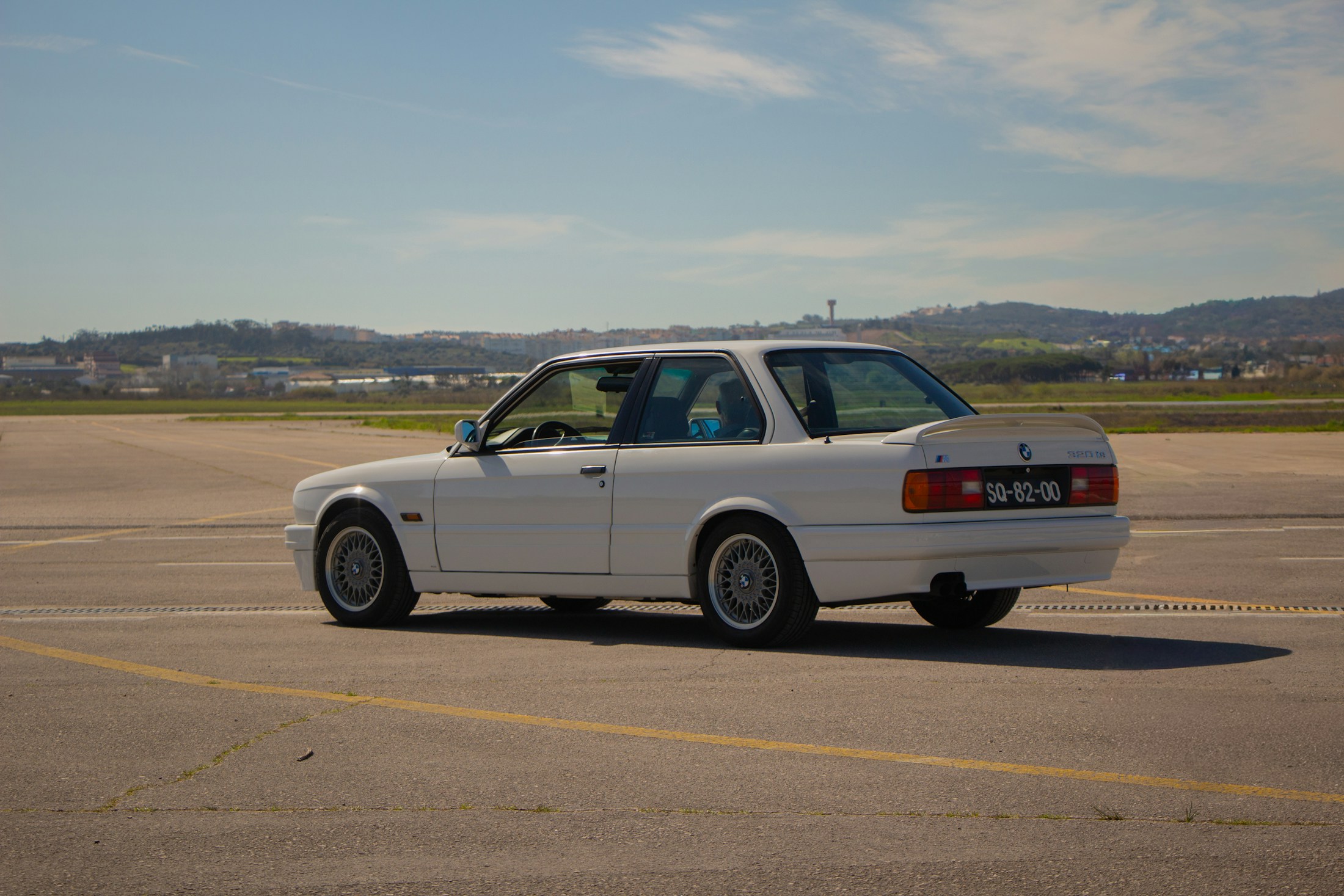 Белый BMW M3 поколения E30 в полном боковом ракурсе на аэродроме